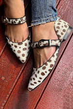 A pair of colorblock instep strap buckle pointy toe flats worn by a person, standing on a wooden floor.